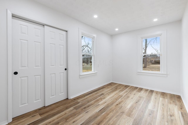 unfurnished bedroom featuring multiple windows, light wood-type flooring, a closet, and recessed lighting