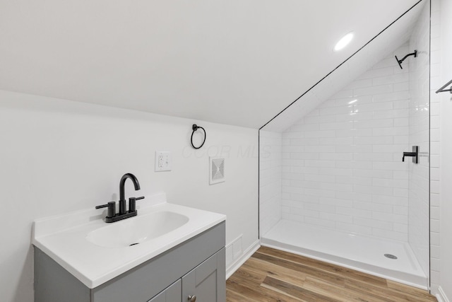 full bathroom with lofted ceiling, wood finished floors, vanity, visible vents, and tiled shower