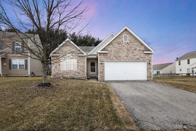 view of front of home featuring driveway, a lawn, stone siding, an attached garage, and fence