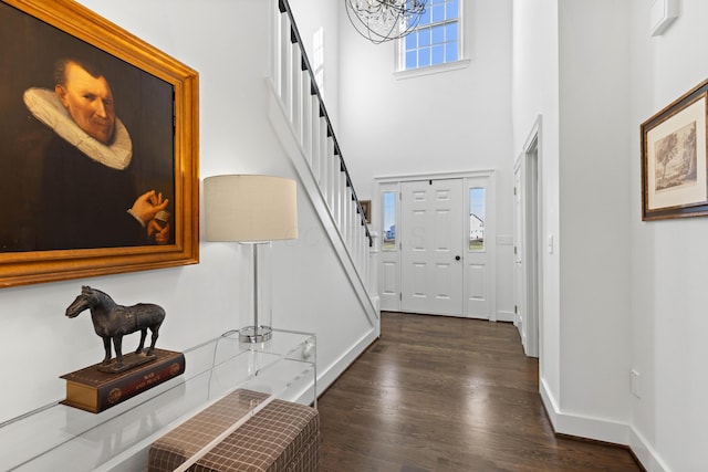 foyer entrance with dark wood-type flooring, a towering ceiling, baseboards, a chandelier, and stairs