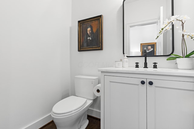 half bath with vanity, toilet, wood finished floors, and baseboards