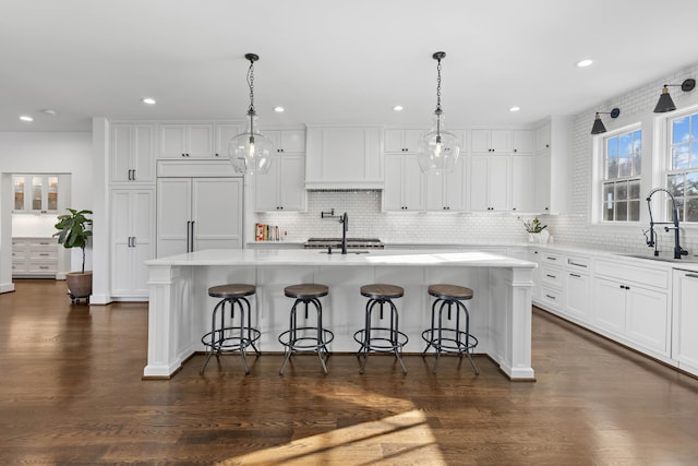 kitchen featuring a center island with sink, a sink, white cabinetry, paneled built in fridge, and light countertops
