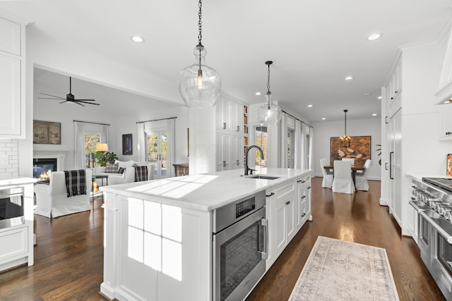 kitchen with a kitchen island with sink, open floor plan, double oven range, white cabinets, and a sink