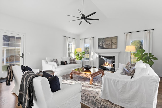 living area featuring a ceiling fan, vaulted ceiling, wood finished floors, and a glass covered fireplace