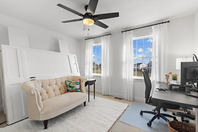 office space featuring light colored carpet, a ceiling fan, visible vents, and baseboards