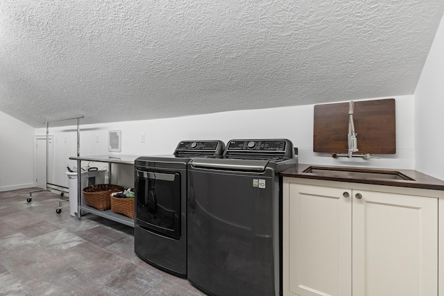 laundry area with washing machine and clothes dryer, cabinet space, a textured ceiling, and a sink