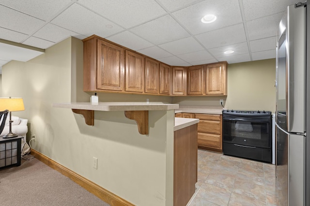 kitchen with a breakfast bar, black electric range oven, freestanding refrigerator, a peninsula, and light countertops