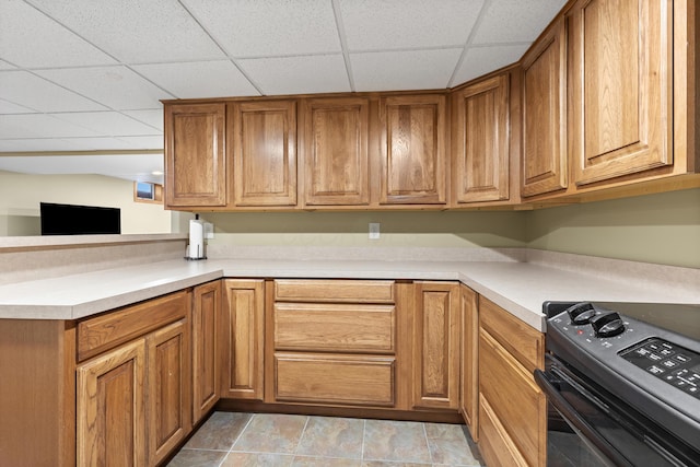 kitchen with black range, a peninsula, brown cabinetry, and light countertops