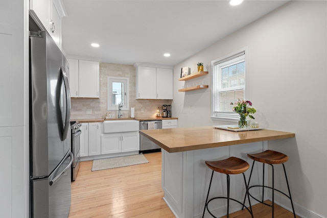 kitchen featuring a peninsula, a sink, wood counters, appliances with stainless steel finishes, and a kitchen bar