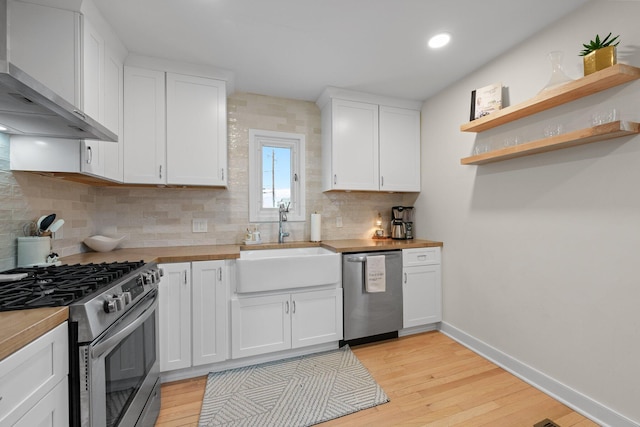 kitchen featuring a sink, white cabinetry, baseboards, appliances with stainless steel finishes, and wall chimney exhaust hood