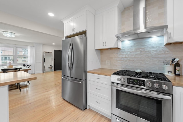 kitchen featuring appliances with stainless steel finishes, white cabinets, light wood-style floors, and wall chimney range hood