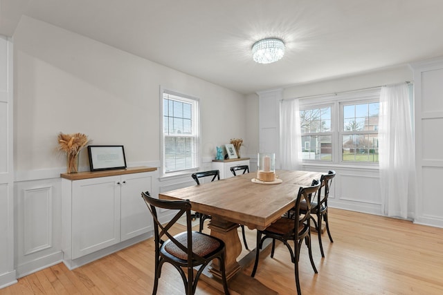 dining room featuring light wood finished floors, a decorative wall, and wainscoting