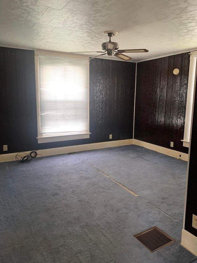 unfurnished room featuring ceiling fan, baseboards, visible vents, and wooden walls