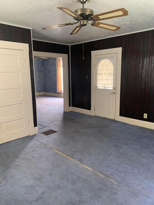 foyer entrance featuring ornamental molding, carpet, ceiling fan, and wooden walls