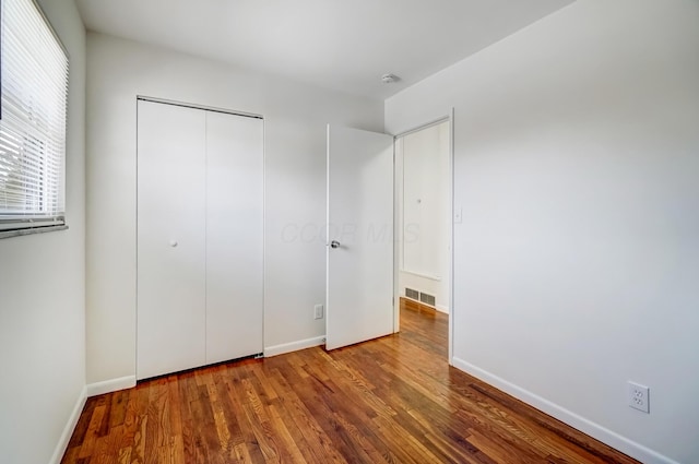 unfurnished bedroom featuring a closet, visible vents, baseboards, and wood finished floors