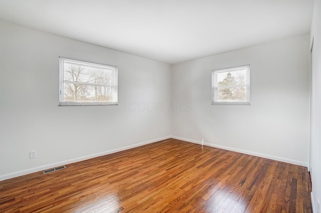 spare room with hardwood / wood-style flooring, baseboards, and visible vents