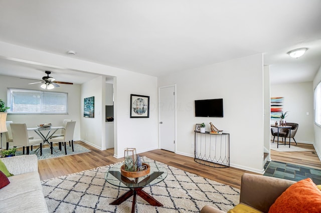 living room with ceiling fan, baseboards, and wood finished floors