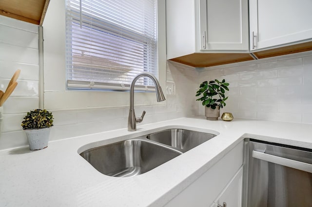 interior details featuring backsplash, dishwasher, white cabinets, and a sink