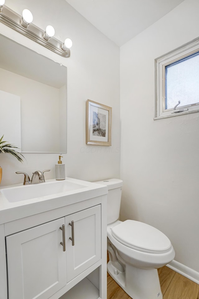 half bathroom featuring toilet, vanity, baseboards, and wood finished floors