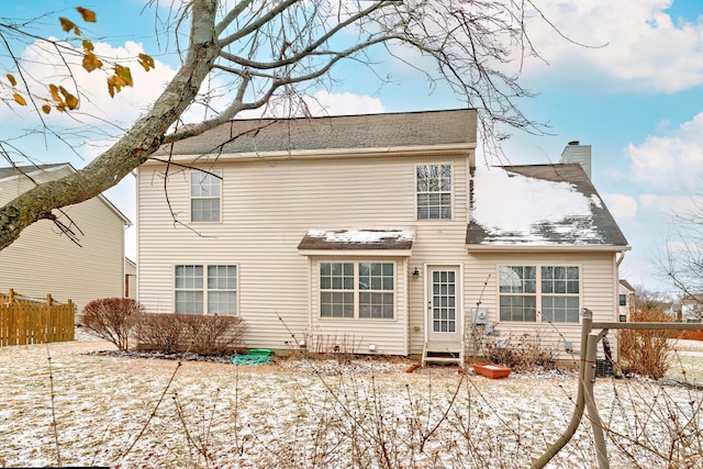 snow covered back of property featuring a chimney and fence