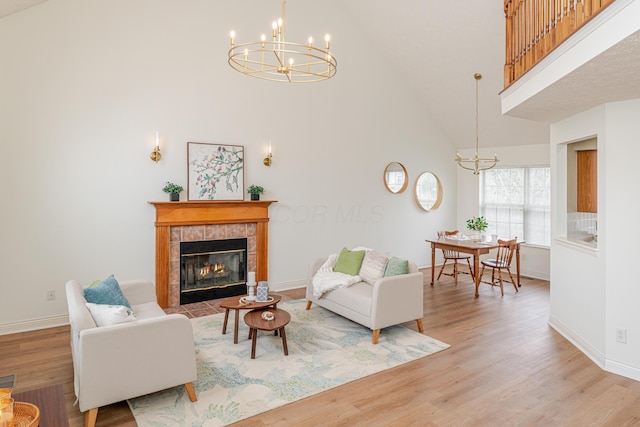 living area featuring a chandelier, high vaulted ceiling, baseboards, light wood finished floors, and a tiled fireplace