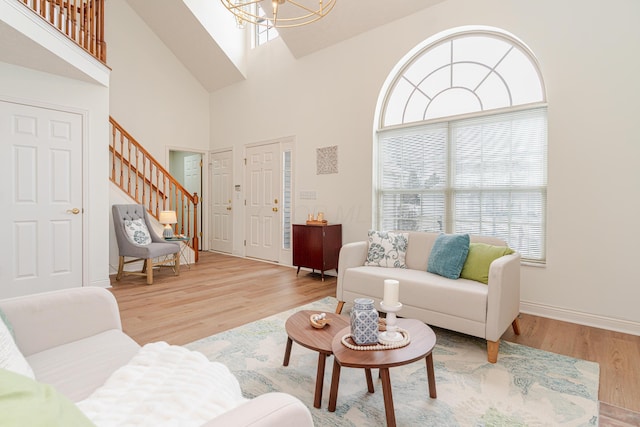 living room featuring a towering ceiling, stairway, an inviting chandelier, wood finished floors, and baseboards