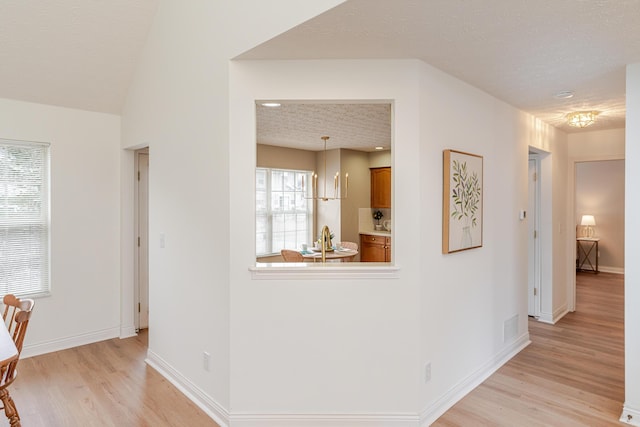 corridor with light wood-type flooring, baseboards, visible vents, and a textured ceiling