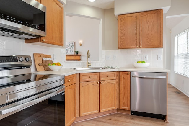 kitchen featuring light wood-style flooring, appliances with stainless steel finishes, a sink, light countertops, and backsplash