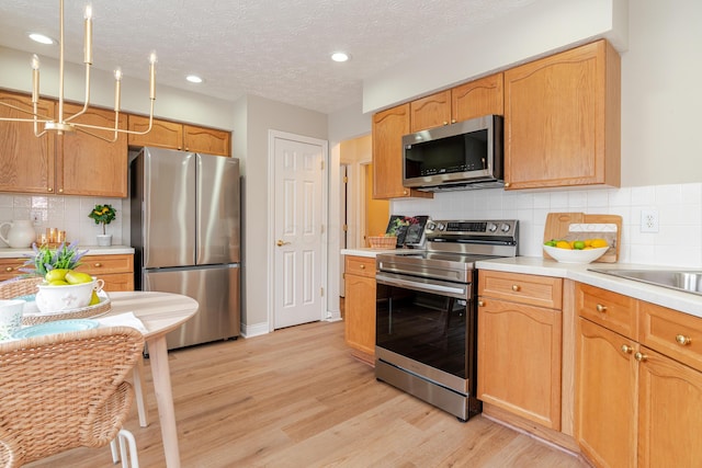 kitchen with a textured ceiling, stainless steel appliances, light countertops, light wood finished floors, and tasteful backsplash