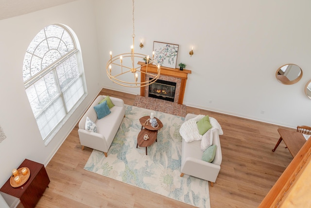 living room featuring a tile fireplace, wood finished floors, a towering ceiling, baseboards, and an inviting chandelier