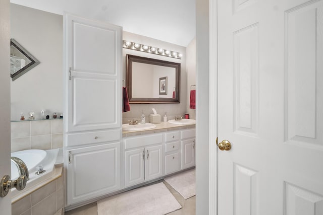 bathroom with a sink, double vanity, tile patterned floors, and tiled bath