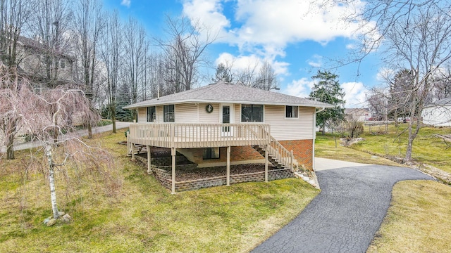 rear view of house with aphalt driveway, brick siding, roof with shingles, a lawn, and stairway