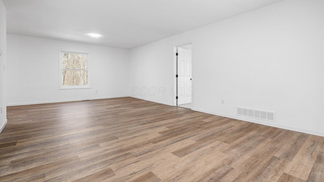 empty room with wood finished floors, visible vents, and baseboards