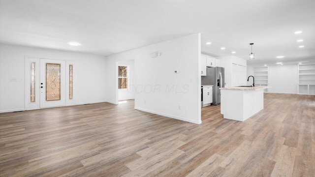 kitchen with open floor plan, white cabinetry, stainless steel refrigerator with ice dispenser, and light wood finished floors