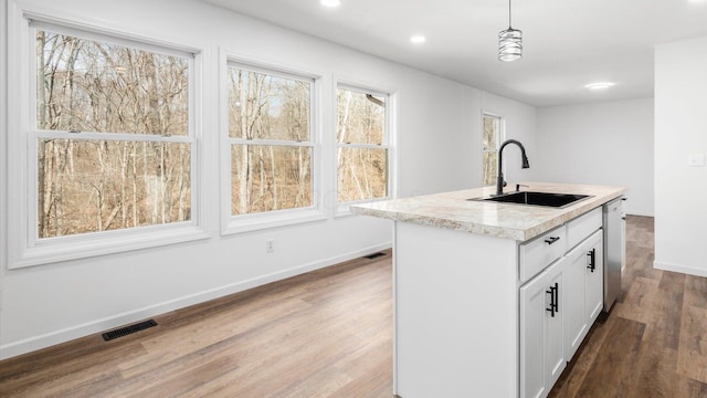 kitchen featuring wood finished floors, a sink, visible vents, baseboards, and decorative light fixtures