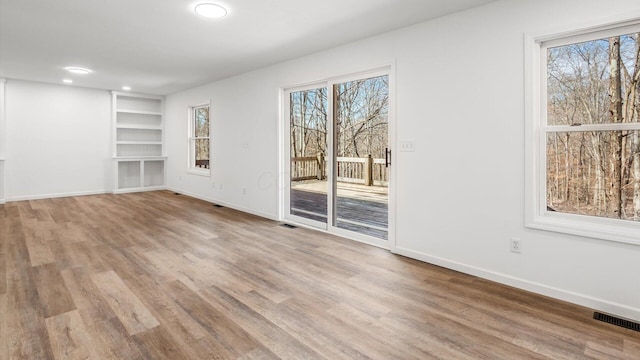 unfurnished room featuring a healthy amount of sunlight, built in features, and wood finished floors