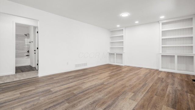 spare room with built in shelves, wood finished floors, visible vents, and baseboards