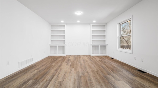 unfurnished room featuring built in shelves, visible vents, baseboards, and wood finished floors