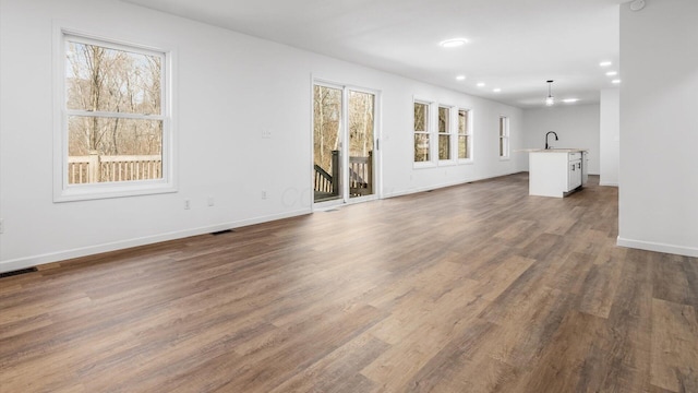 unfurnished living room with dark wood-style floors, visible vents, a sink, and baseboards