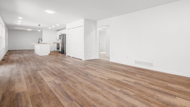 unfurnished living room featuring baseboards, visible vents, light wood-style floors, a sink, and recessed lighting