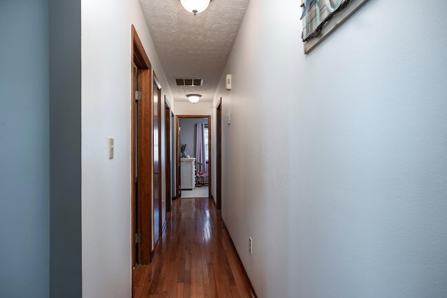 hall featuring attic access, dark wood-style floors, visible vents, and a textured ceiling