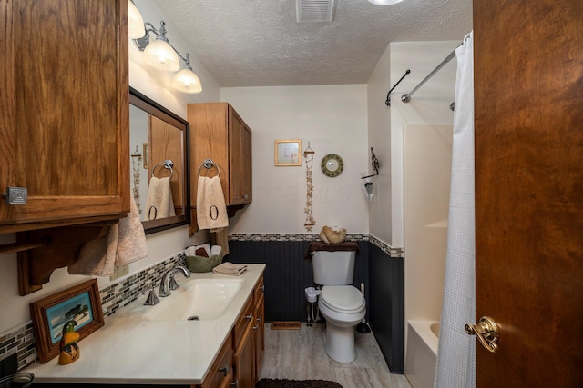 full bath with vanity, a textured ceiling, visible vents, wainscoting, and toilet