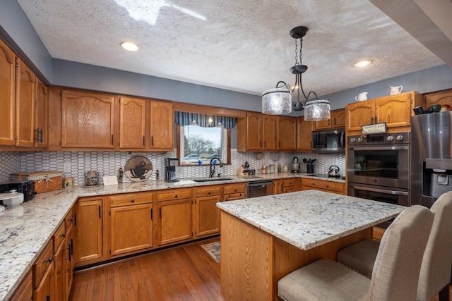 kitchen featuring a breakfast bar, dark wood finished floors, a sink, appliances with stainless steel finishes, and brown cabinets