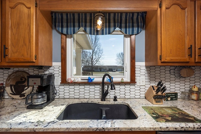 kitchen featuring a sink, light stone countertops, backsplash, and brown cabinetry