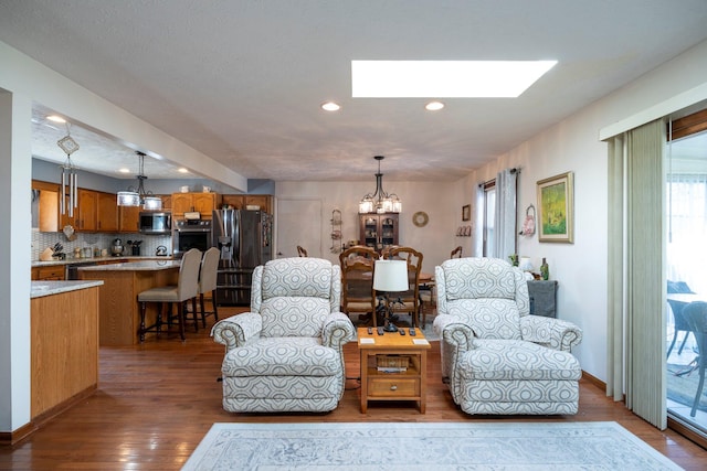 living area with a skylight, an inviting chandelier, wood finished floors, and a healthy amount of sunlight