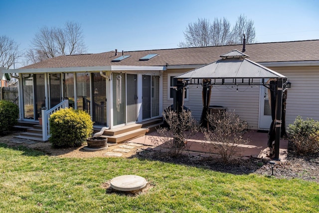 rear view of property featuring a shingled roof, a gazebo, a lawn, a sunroom, and a patio area