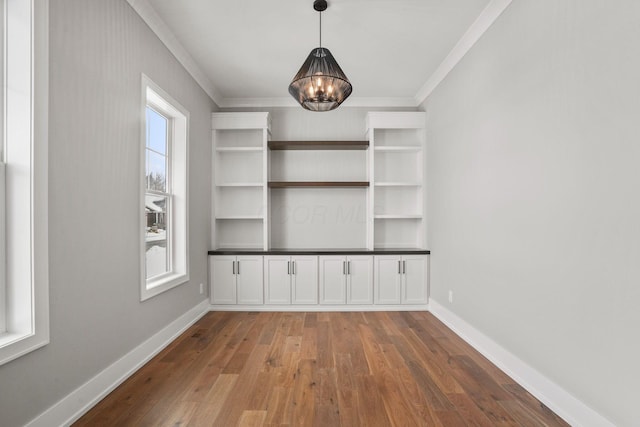 interior space with crown molding, a chandelier, hardwood / wood-style flooring, and baseboards