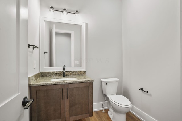 half bathroom featuring toilet, baseboards, wood finished floors, and vanity