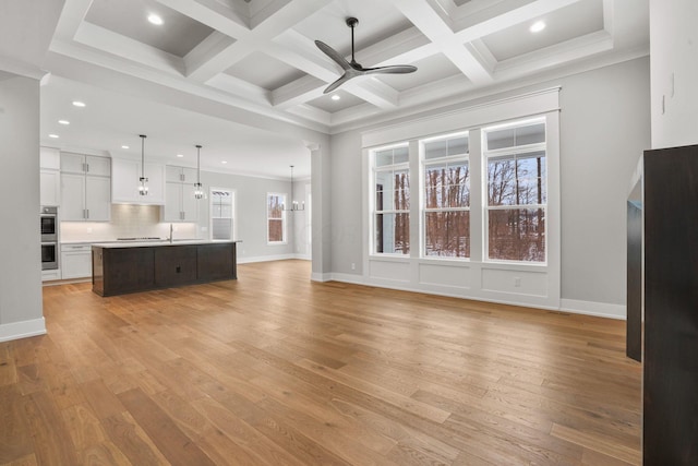 unfurnished living room featuring ceiling fan with notable chandelier, light wood-type flooring, coffered ceiling, and baseboards