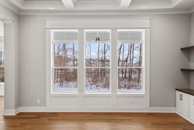 interior space featuring baseboards, coffered ceiling, wood finished floors, and ornamental molding